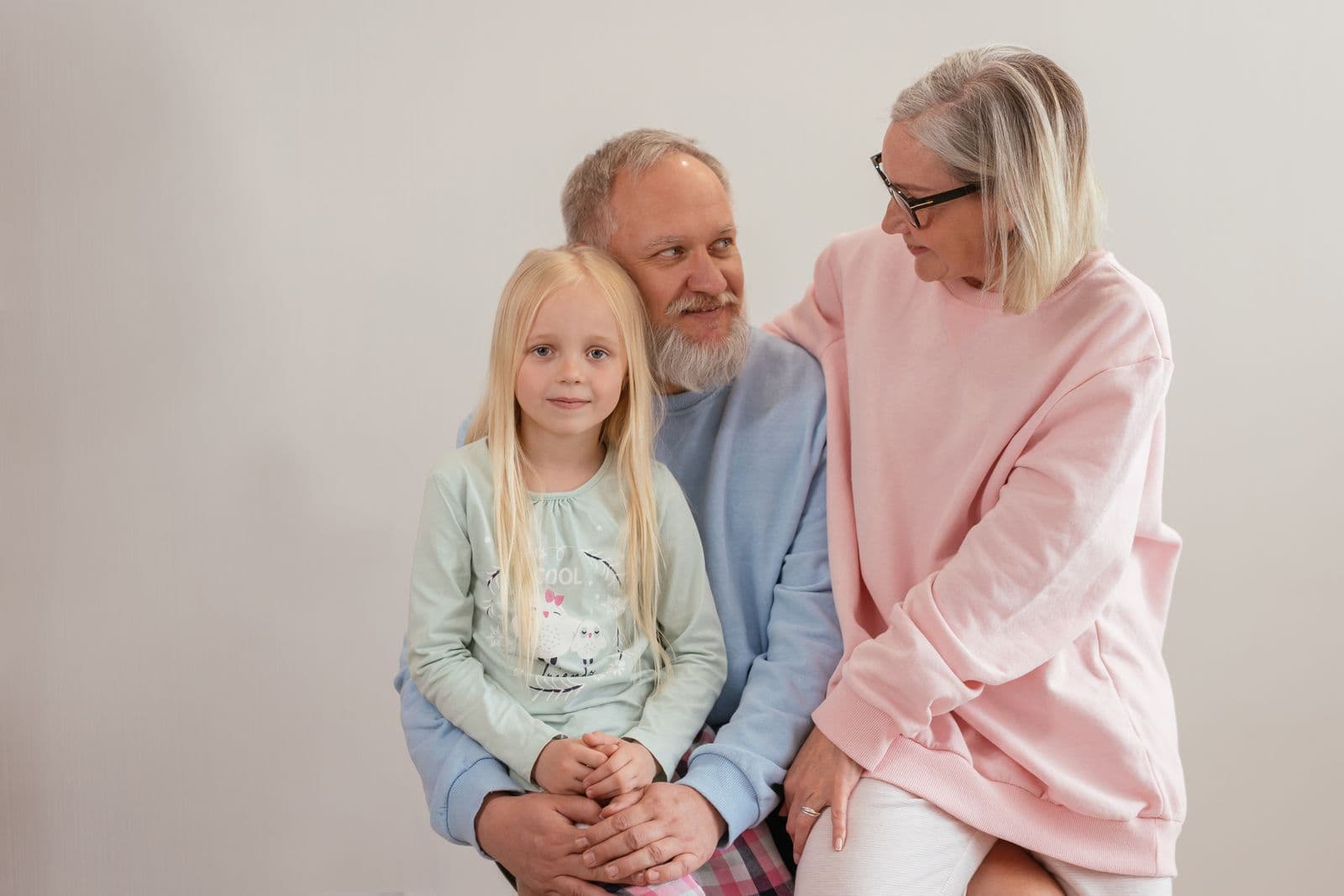 Two smiling grandparents in soft pastel sweaters sitting with their young granddaughter.