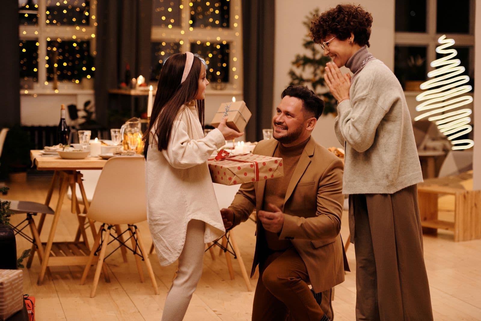 A girl hands wrapped presents to her dad at a warm family Christmas gathering.