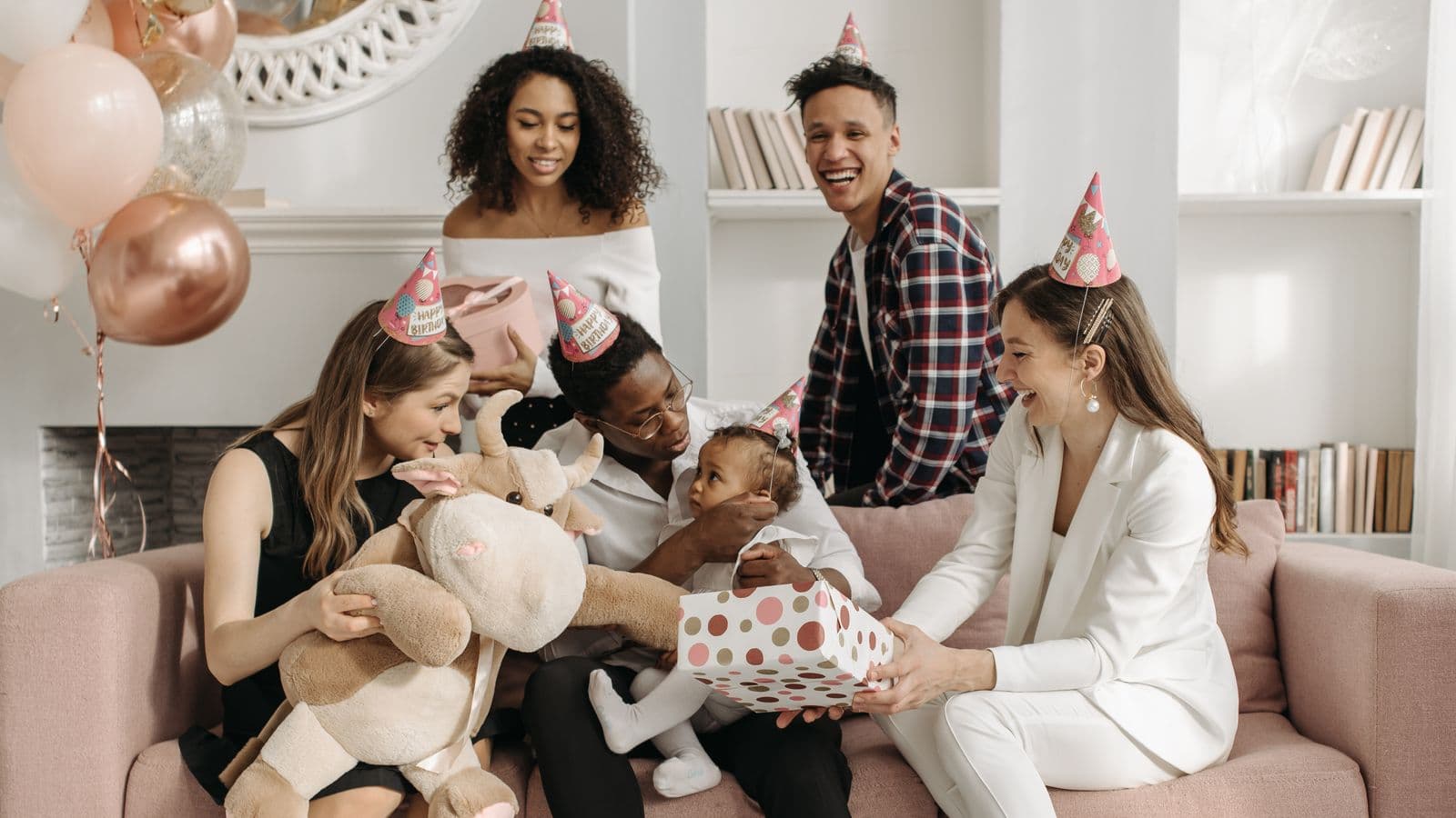 A family gathered on a rose-pink couch, smiling as one relative hands over a big wrapped gift the whole group chipped in on.
