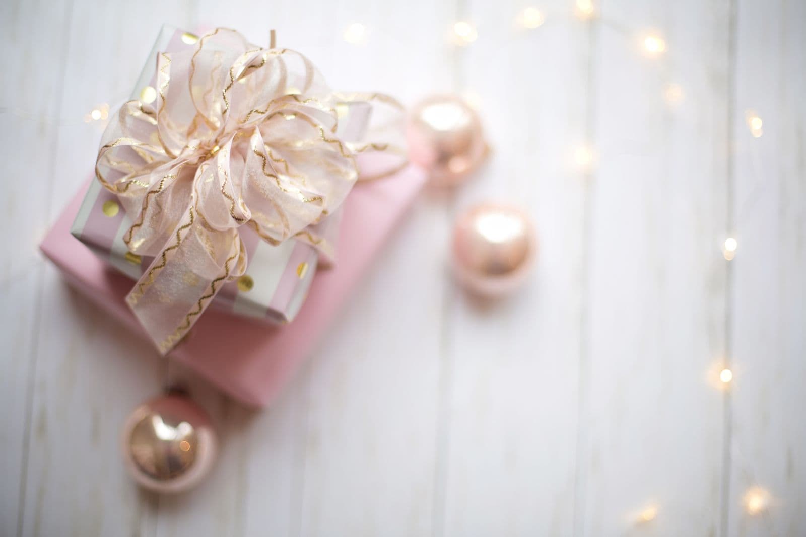 A pastel-pink wrapped gift with a soft ribbon bow on a light table.